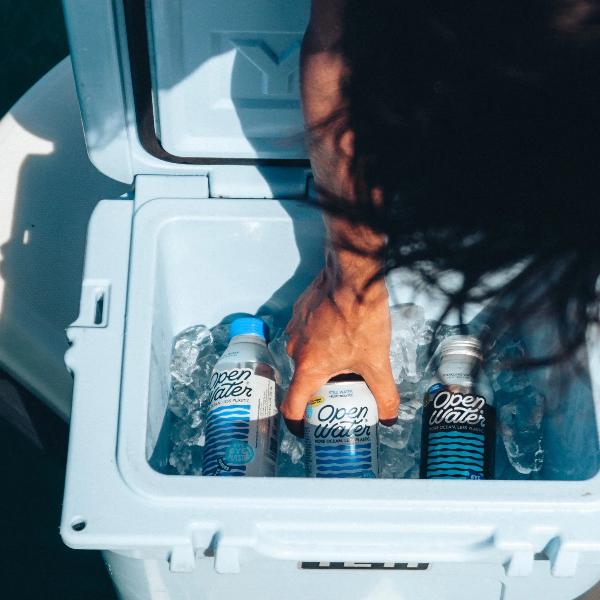 person grabbing Open Water canned water out of cooler with ice