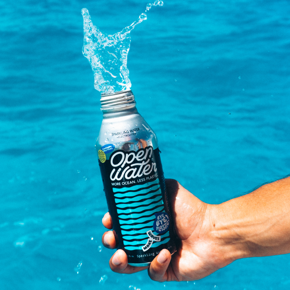 Sparkling water in aluminum bottle splashing by the ocean